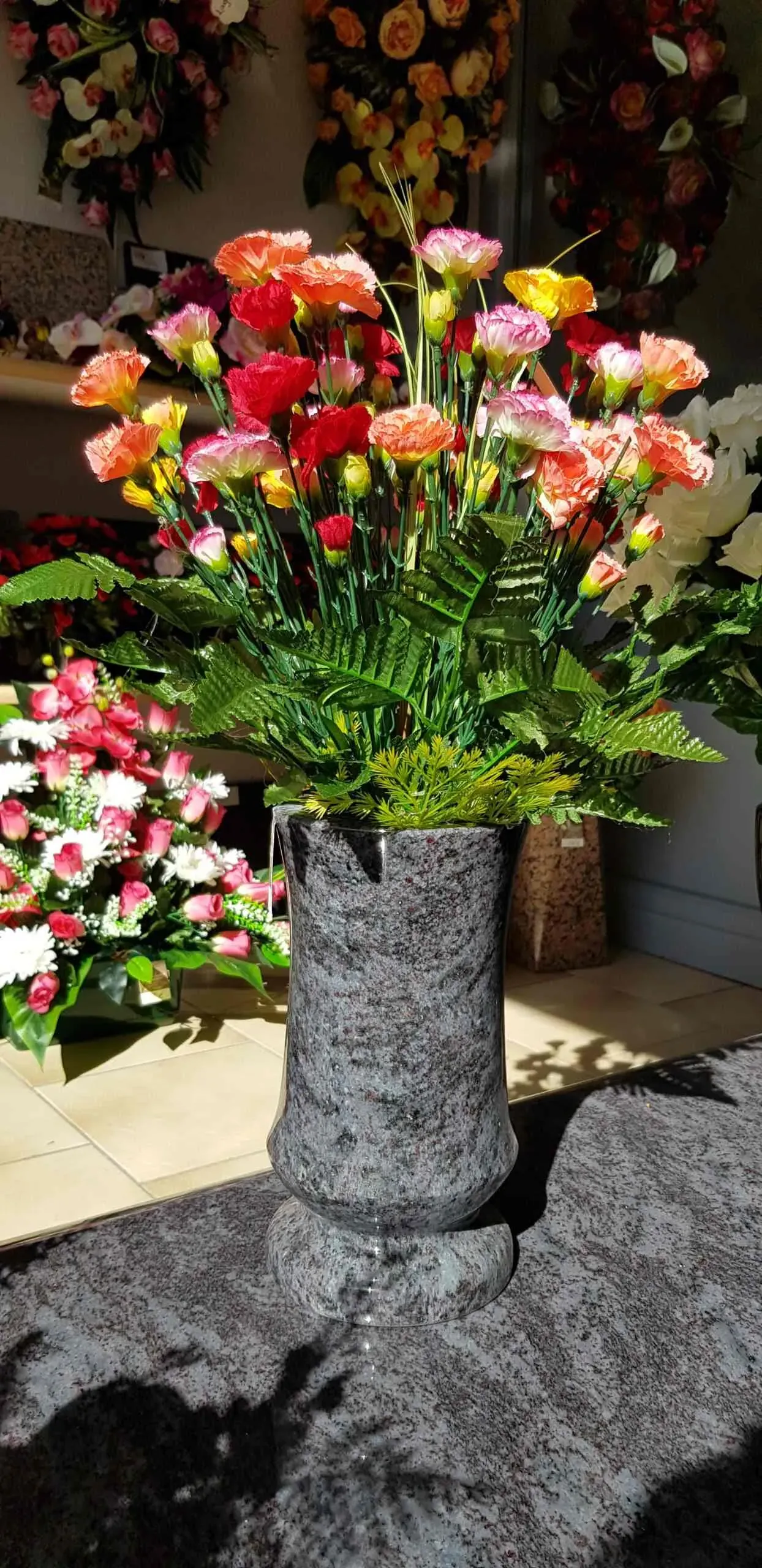 Vase funéraire en granit gris garni d'un bouquet d'œillets multicolores